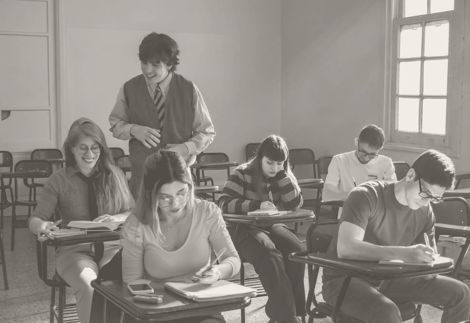 Students working at their desks in a bright classroom while a teacher moves between them